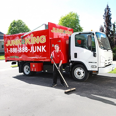 Junk King professional standing beside a branded dump truck using a push broom.