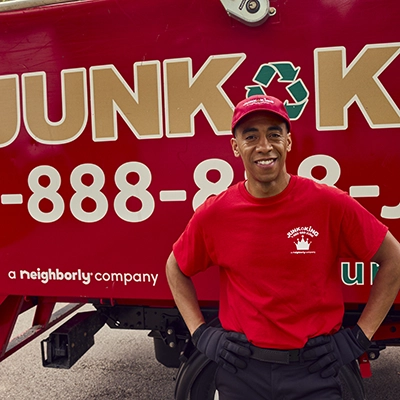 Junk King professional standing by a red branded truck with hands on his hips.