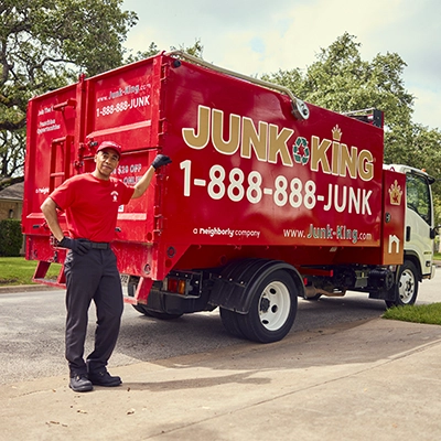 Junk King professional leaning against a red branded dump truck.