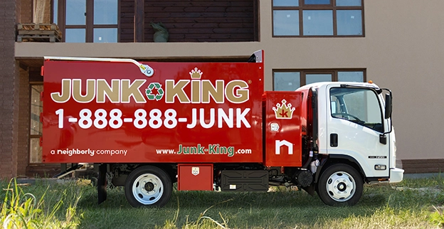 A branded Junk King dump truck parked outside of a building under construction.
