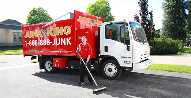 A Junk King professional using a push broom beside a branded dump truck.