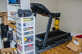 A room in a house with a treadmill and storage containers.