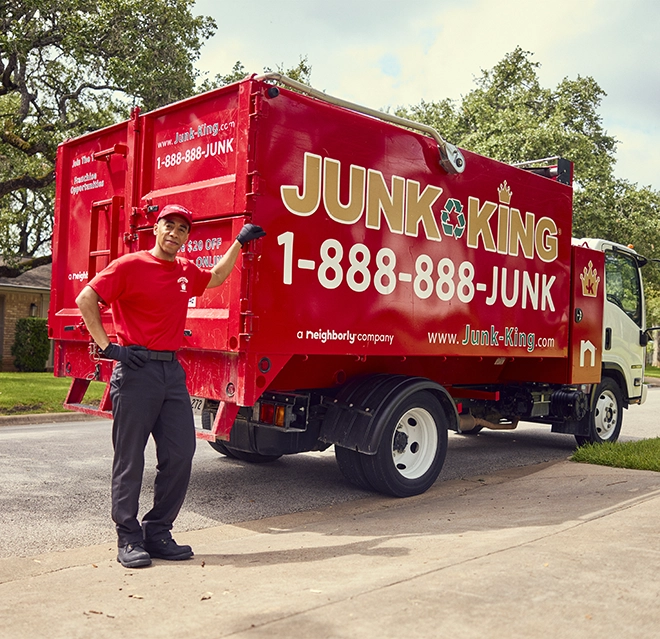 Junk King professional leaning his arm against a red Junk King dumpster truck.