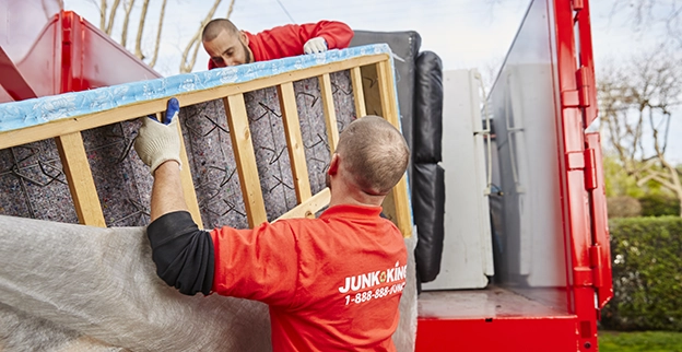 Two Junk King professionals loading a mattress onto a truck.