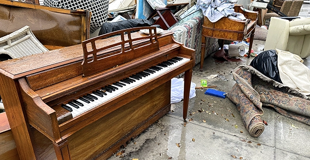An old piano sitting outside with a pile of junk.
