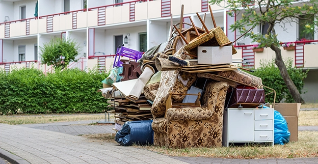 Large pile of furniture and junk outside of an apartment complex.