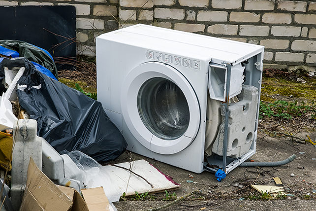 An old washing machine sitting outside of a brick home.