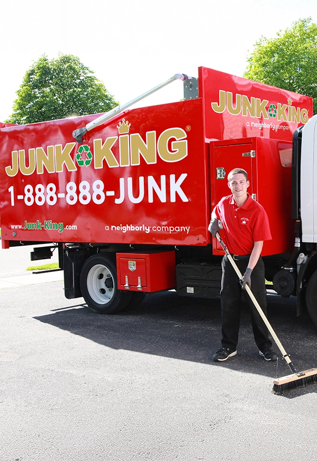 Junk King professional standing beside a dump truck with a push broom.