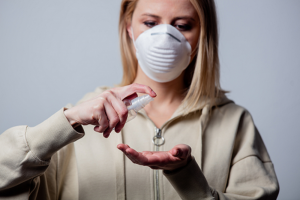 woman wearing grey hoodie and white face mask spraying hand sanitizer