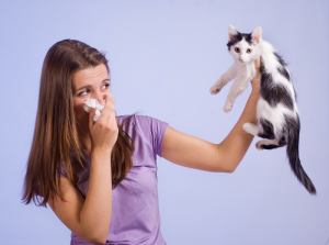 Female holding tissue to face in one hand and a cat held high in the other hand