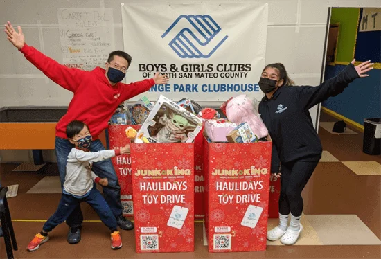Family happily standing with Junk King Haulidays Toy Drive bins.
