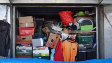 Cluttered storage unit filled with boxes, clothes, and household items.