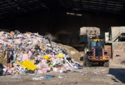 Bulldozer pushing a pile of garbage inside a facility.