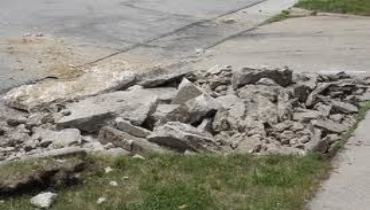 Piles of broken concrete rubble on a grassy area near a street.