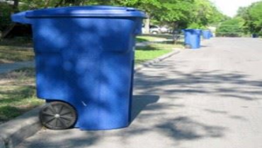 A blue trash can positioned on the side of a street.