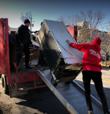 Workers loading an old refrigerator onto a Junk King truck.