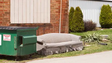 Old furniture outside beside a trash dumpster ready to be recycled